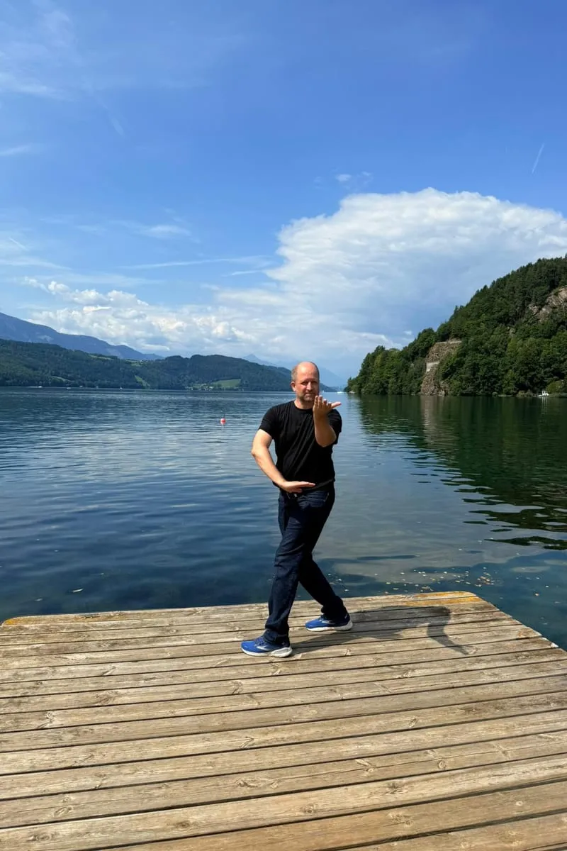 Christian Weidl in a Qi Gong posture by the lakeshore — calm stance, focused breath